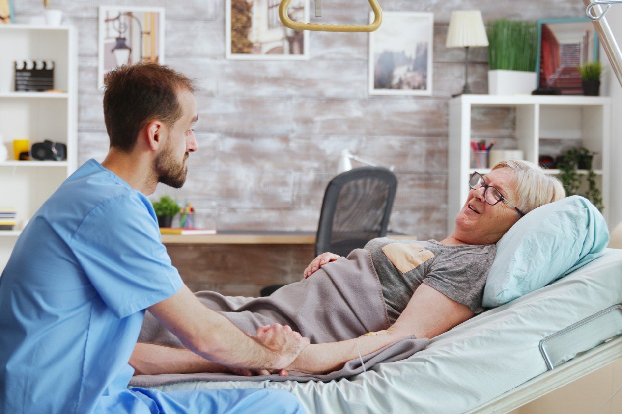 bedridden elderly woman getting helped by male caretaker